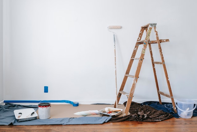 A room set up to be painted, with a tarp on the floor, a ladder, and a paint roller